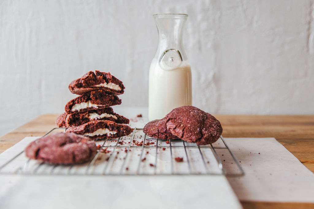 Red velvet cookies stuffed with cheesecake beside a bottle of milk